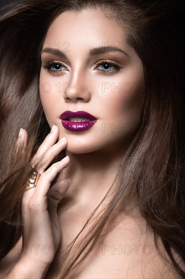 Beautiful girl with golden makeup and burgundy lips with the wind in hair. Beauty face. Picture taken in the studio on a black background