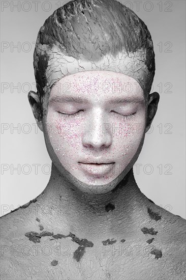 Young man with art creative make-up with mud on his face. Cosmetic mask. Beauty face. Picture taken in the studio on a black background
