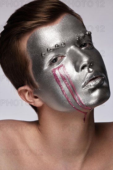 Young man with art creative art make-up with silver paint on his face. Beauty face. Picture taken in the studio on a white background