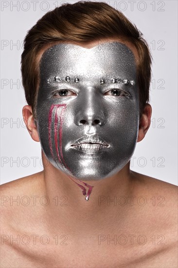Young man with art creative art make-up with silver paint on his face. Beauty face. Picture taken in the studio on a white background