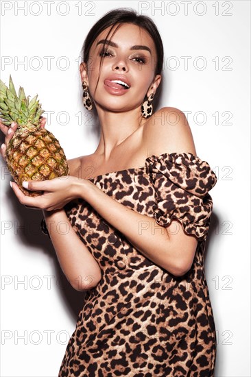 Beautiful sexy woman with pineapple in hands in a leopard dress and earrings