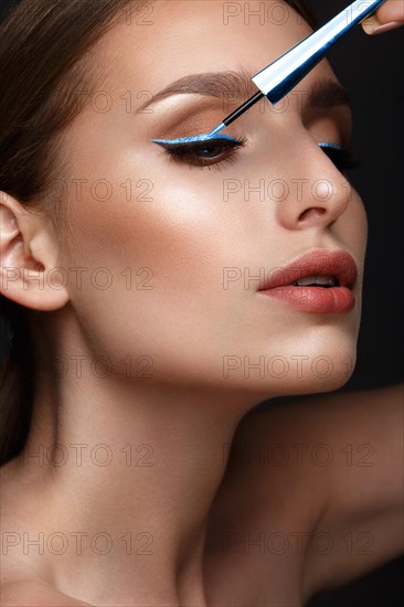 Beautiful girl with sexy lips and classic makeup with cosmetic blue eyeliner in hand. Beauty face. Photo taken in the studio