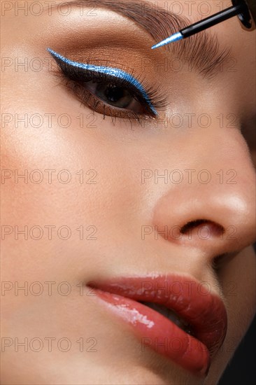 Beautiful girl with sexy lips and classic makeup with cosmetic blue eyeliner in hand. Beauty face. Photo taken in the studio