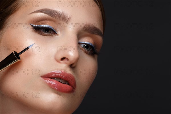 Beautiful girl with sexy lips and classic makeup with cosmetic blue eyeliner in hand. Beauty face. Photo taken in the studio