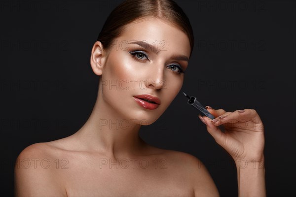 Beautiful girl with sexy lips and classic makeup with cosmetic blue eyeliner in hand. Beauty face. Photo taken in the studio