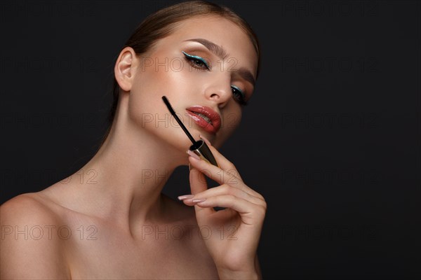 Beautiful girl with sexy lips and classic makeup with cosmetic mascara brush in hand. Beauty face. Photo taken in the studio