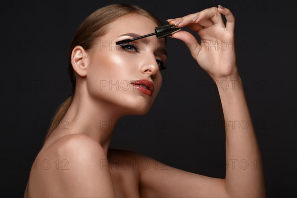 Beautiful girl with sexy lips and classic makeup with cosmetic mascara brush in hand. Beauty face. Photo taken in the studio