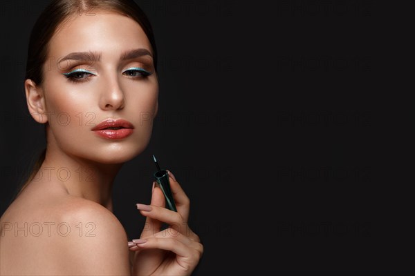 Beautiful girl with sexy lips and classic makeup with cosmetic blue eyeliner in hand. Beauty face. Photo taken in the studio