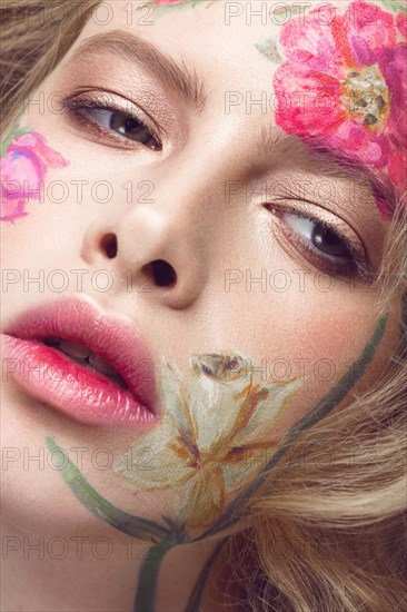 Beautiful blond girl with tresses and a floral pattern on the face. Beauty flowers. Portrait shot in studio