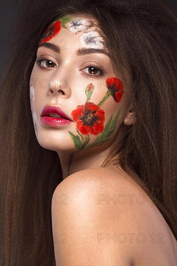 Beautiful brunette girl with curls and a floral pattern on the face. Beauty flowers. Portrait shot in studio