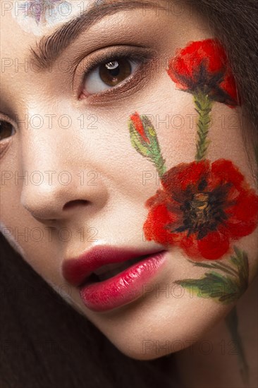 Beautiful brunette girl with curls and a floral pattern on the face. Beauty flowers. Portrait shot in studio