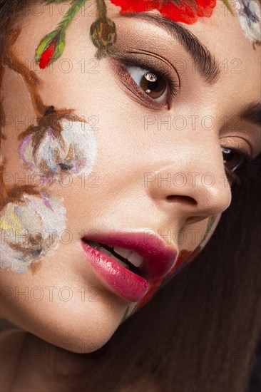 Beautiful brunette girl with curls and a floral pattern on the face. Beauty flowers. Portrait shot in studio