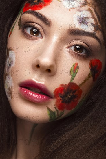 Beautiful brunette girl with curls and a floral pattern on the face. Beauty flowers. Portrait shot in studio