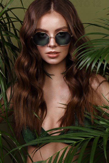 Beautiful sexy woman in a bikini posing in the middle of green plants. Summer look. Beauty face. Photo taken in the studio