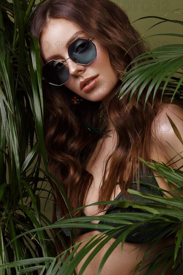 Beautiful sexy woman in a bikini posing in the middle of green plants. Summer look. Beauty face. Photo taken in the studio