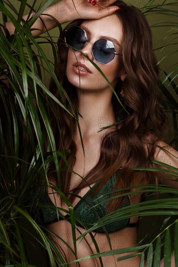 Beautiful sexy woman in a bikini posing in the middle of green plants. Summer look. Beauty face. Photo taken in the studio