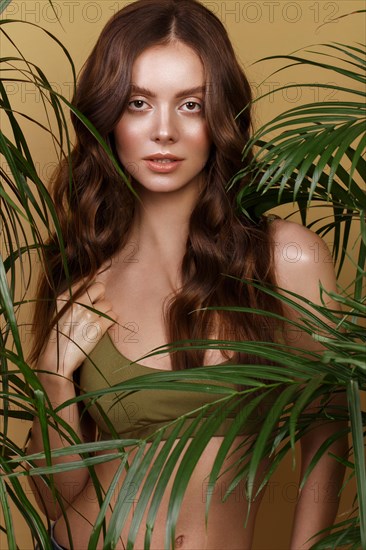 Beautiful sexy woman in a bikini posing in the middle of green plants. Summer look. Beauty face. Photo taken in the studio