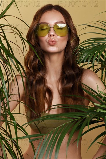 Beautiful sexy woman in a bikini posing in the middle of green plants. Summer look. Beauty face. Photo taken in the studio