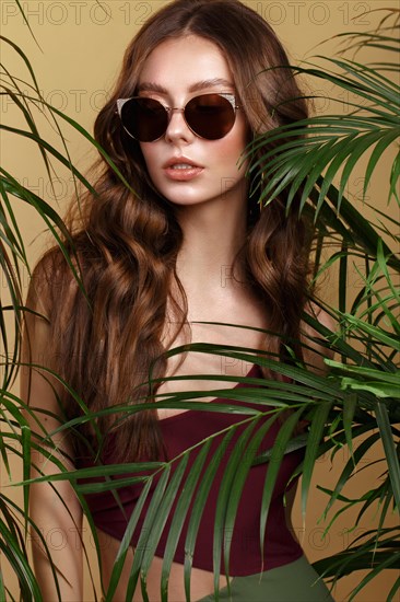 Beautiful sexy woman in a bikini and sunglasses posing in the middle of green plants. Summer look. Beauty face. Photo taken in the studio