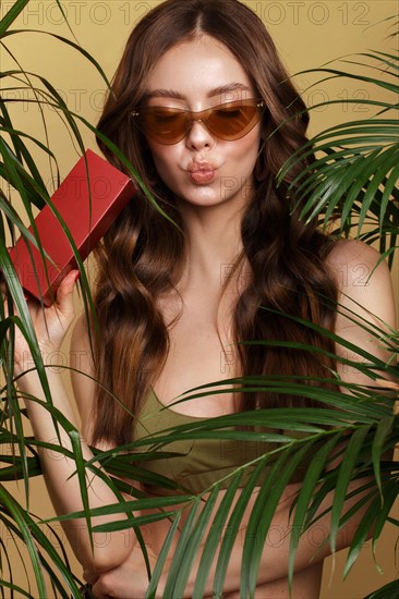 Beautiful sexy woman in a bikini posing in the middle of green plants with a box of cosmetics in hand. Summer look. Beauty face. Photo taken in the studio