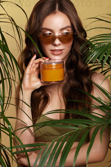 Beautiful sexy woman in a bikini posing in the middle of green plants with a box of cosmetics in hand. Summer look. Beauty face. Photo taken in the studio