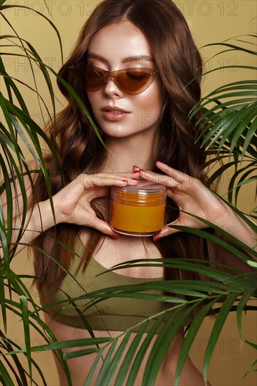 Beautiful sexy woman in a bikini posing in the middle of green plants with a box of cosmetics in hand. Summer look. Beauty face. Photo taken in the studio