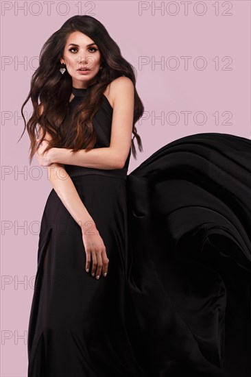 Beautiful brunette woman with curls and classic make-up in a flying black dress. Beauty face. Photo taken in studio