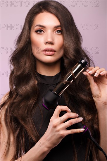 Beautiful brunette woman with curls and classic make-up in a black dress with a hair dryer in hands. Beauty face. Photo taken in studio