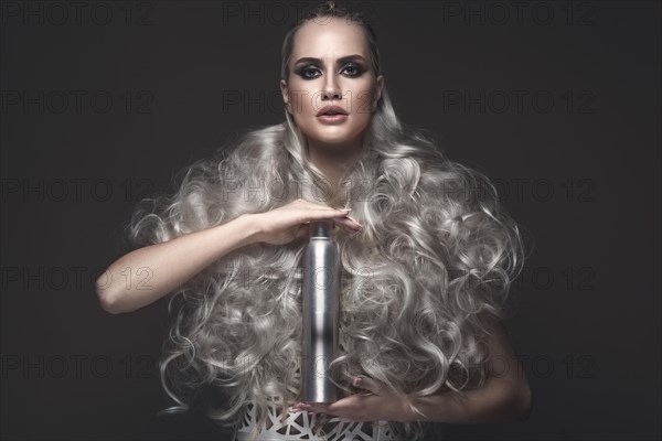 Beautiful girl in art dress and avant-garde hairstyles with cosmetic products in her hands. Beauty face. Photos shot in the studio