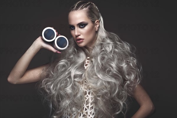 Beautiful girl in art dress and avant-garde hairstyles with cosmetic products in her hands. Beauty face. Photos shot in the studio