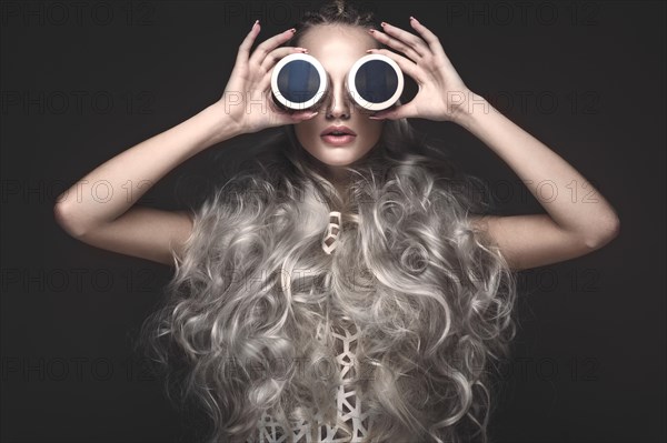 Beautiful girl in art dress and avant-garde hairstyles with cosmetic products in her hands. Beauty face. Photos shot in the studio