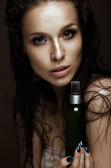 Beautiful girl with a bright make-up and wet hair and skin with bottle of cosmetic products in the hands. Beauty face. Picture taken in the studio on a black background
