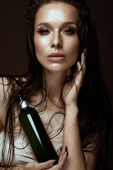 Beautiful girl with a bright make-up and wet hair and skin with bottle of cosmetic products in the hands. Beauty face. Picture taken in the studio on a black background