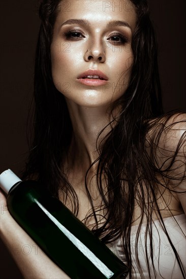 Beautiful girl with a bright make-up and wet hair and skin with bottle of cosmetic products in the hands. Beauty face. Picture taken in the studio on a black background