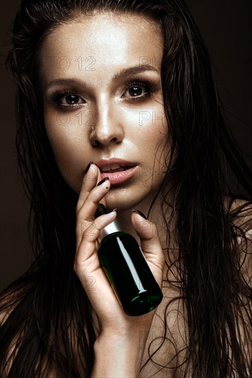 Beautiful girl with a bright make-up and wet hair and skin with bottle of cosmetic products in the hands. Beauty face. Picture taken in the studio on a black background