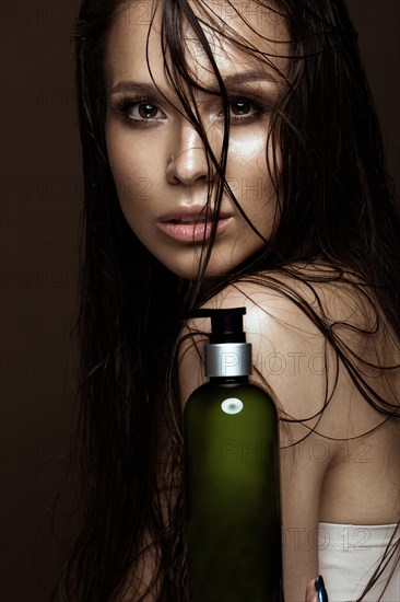 Beautiful girl with a bright make-up and wet hair and skin with bottle of cosmetic products in the hands. Beauty face. Picture taken in the studio on a black background