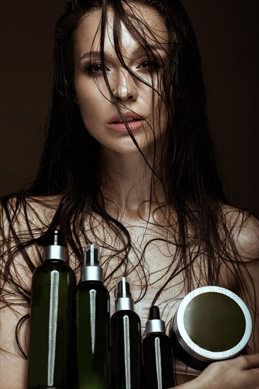 Beautiful girl with a bright make-up and wet hair and skin with bottle of cosmetic products in the hands. Beauty face. Picture taken in the studio on a black background