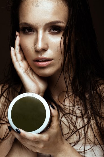 Beautiful girl with a bright make-up and wet hair and skin with bottle of cosmetic products in the hands. Beauty face. Picture taken in the studio on a black background