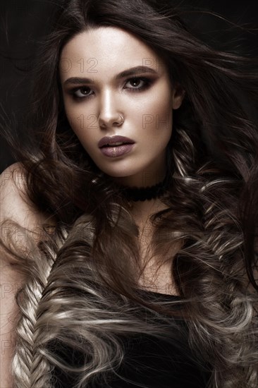 Brunette girl with a creative hairstyle braids and dark make-up. Beauty face. Photo taken in the studio