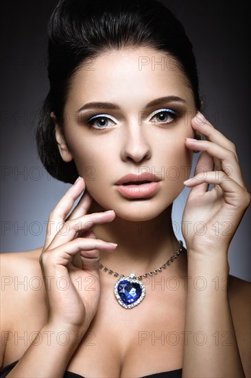 Beautiful brunette with a bright evening make-up with a necklace Heart of the Ocean. Picture taken in the studio on a gray background