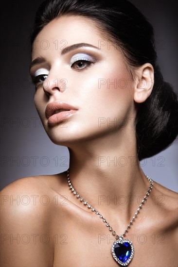 Beautiful brunette with a bright evening make-up with a necklace Heart of the Ocean. Picture taken in the studio on a gray background