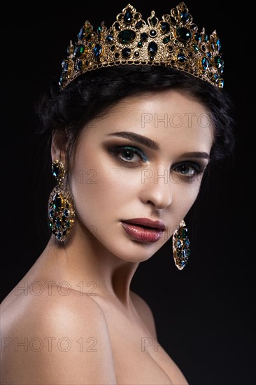 Beautiful brunette girl with a golden crown and earrings and professional evening make-up. Beauty face. Picture taken in the studio