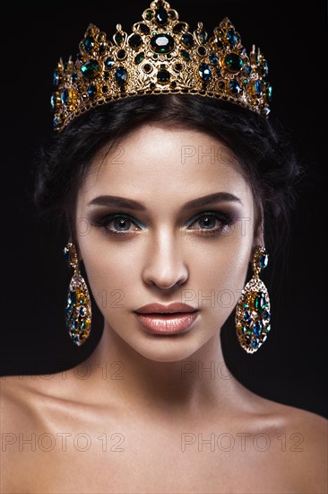 Beautiful brunette girl with a golden crown and earrings and professional evening make-up. Beauty face. Picture taken in the studio