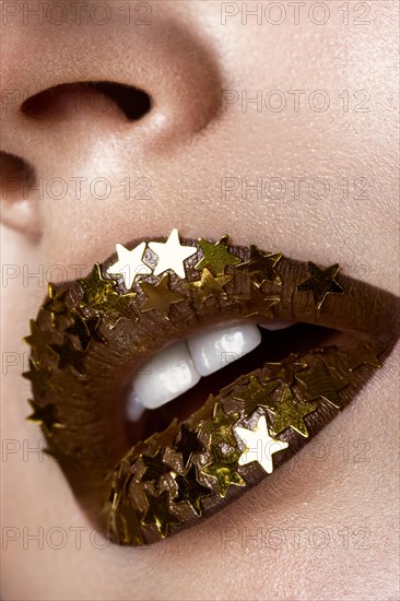 Beautiful girl with a golden shiny stars on her lips. Beauty face. Photo taken in the studio