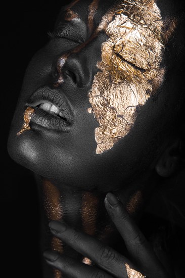 Fashion portrait of a dark-skinned girl with gold make-up.Beauty face. Picture taken in the studio on a black background