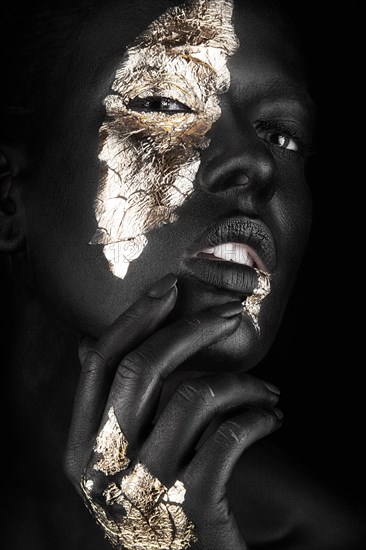 Fashion portrait of a dark-skinned girl with gold make-up.Beauty face. Picture taken in the studio on a black background