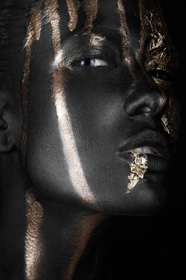 Fashion portrait of a dark-skinned girl with gold make-up.Beauty face. Picture taken in the studio on a black background