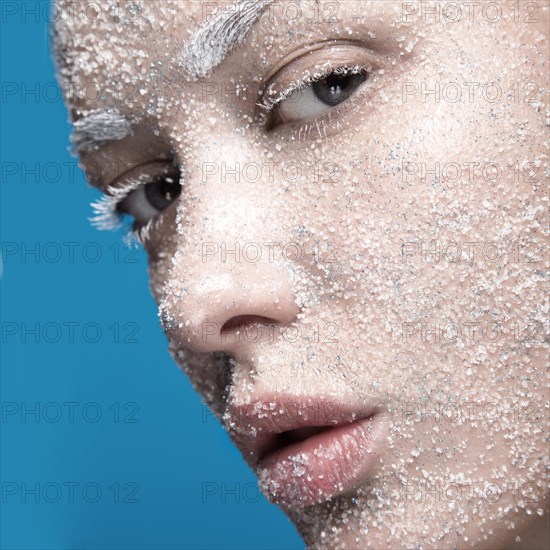 Portrait of a girl with pale skin and sugar snow on her face. Creative art beauty fashion. Picture taken in the studio on a blue background