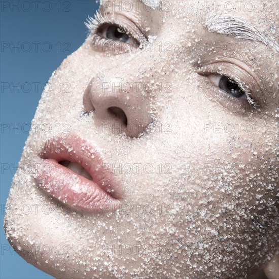 Portrait of a girl with pale skin and sugar snow on her face. Creative art beauty fashion. Picture taken in the studio on a blue background