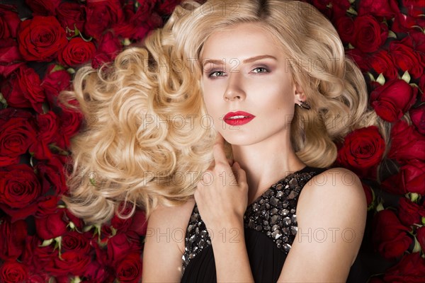 Beautiful blond girl lying on a background of roses. Curls